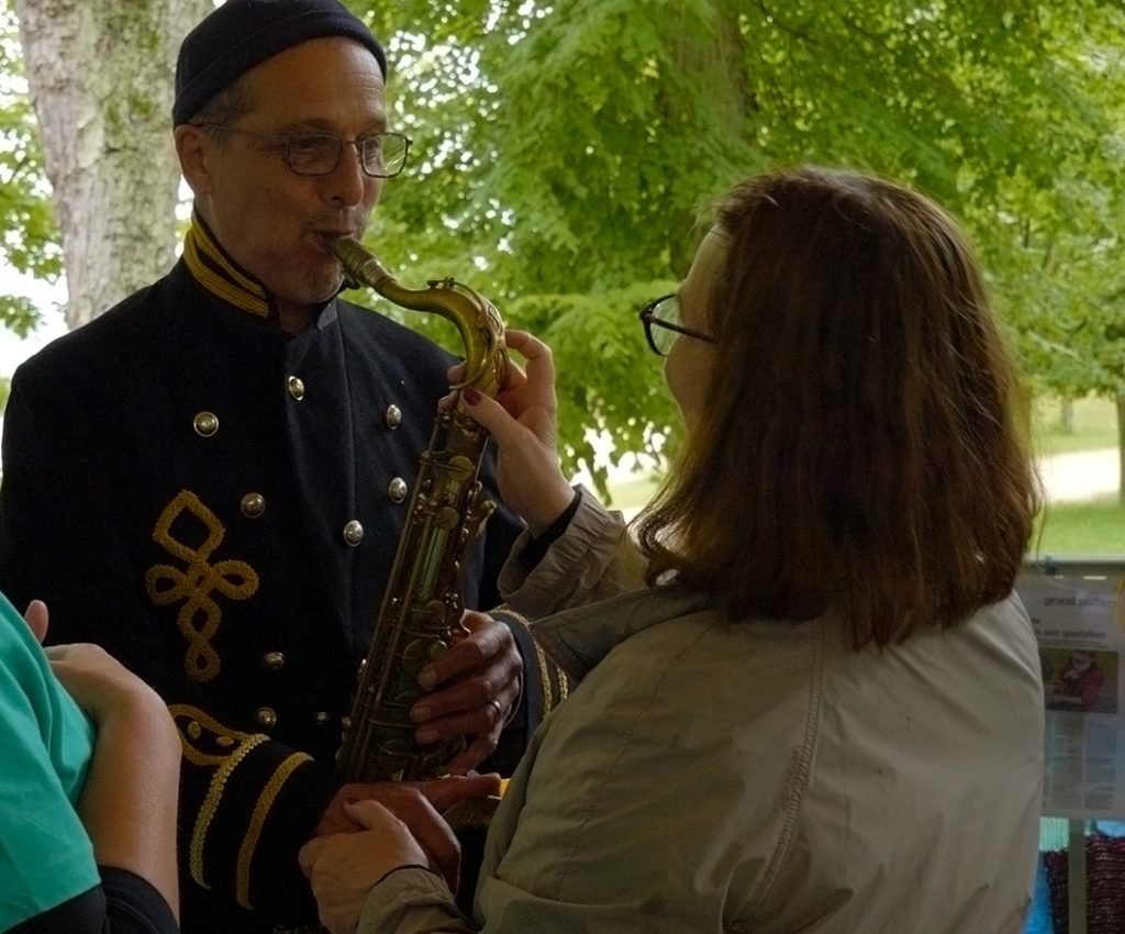 1 photo d'un musicien saxophoniste en train de jouer, pendant qu'une dame sourdaveugle touche son instrument de musique