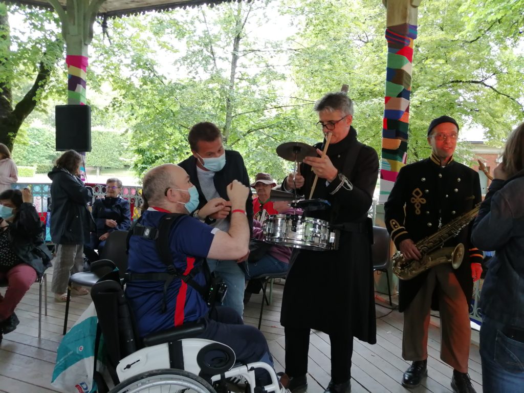 1 photo d'un musicien percussionniste en train de jouer, pendant qu'un homme sourdaveugle touche son instrument de musique