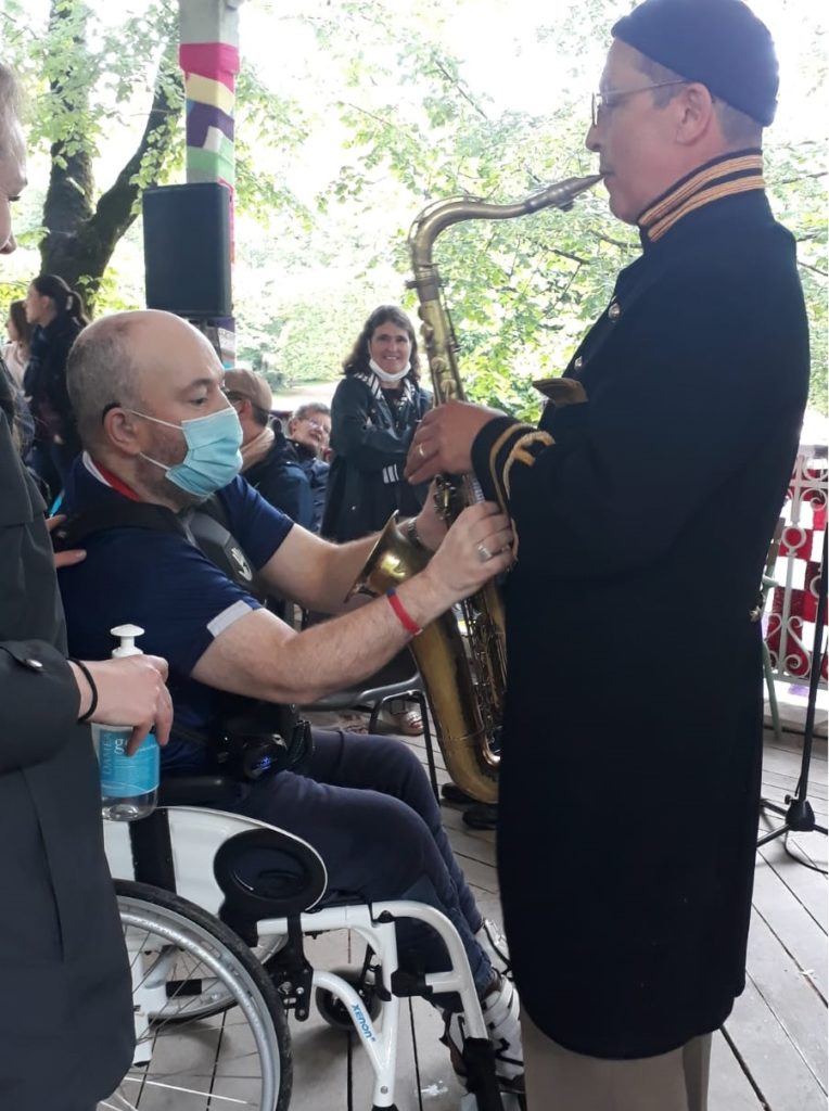 1 photo d'un musicien saxophoniste en train de jouer, pendant qu'un homme sourdaveugle touche son instrument de musique